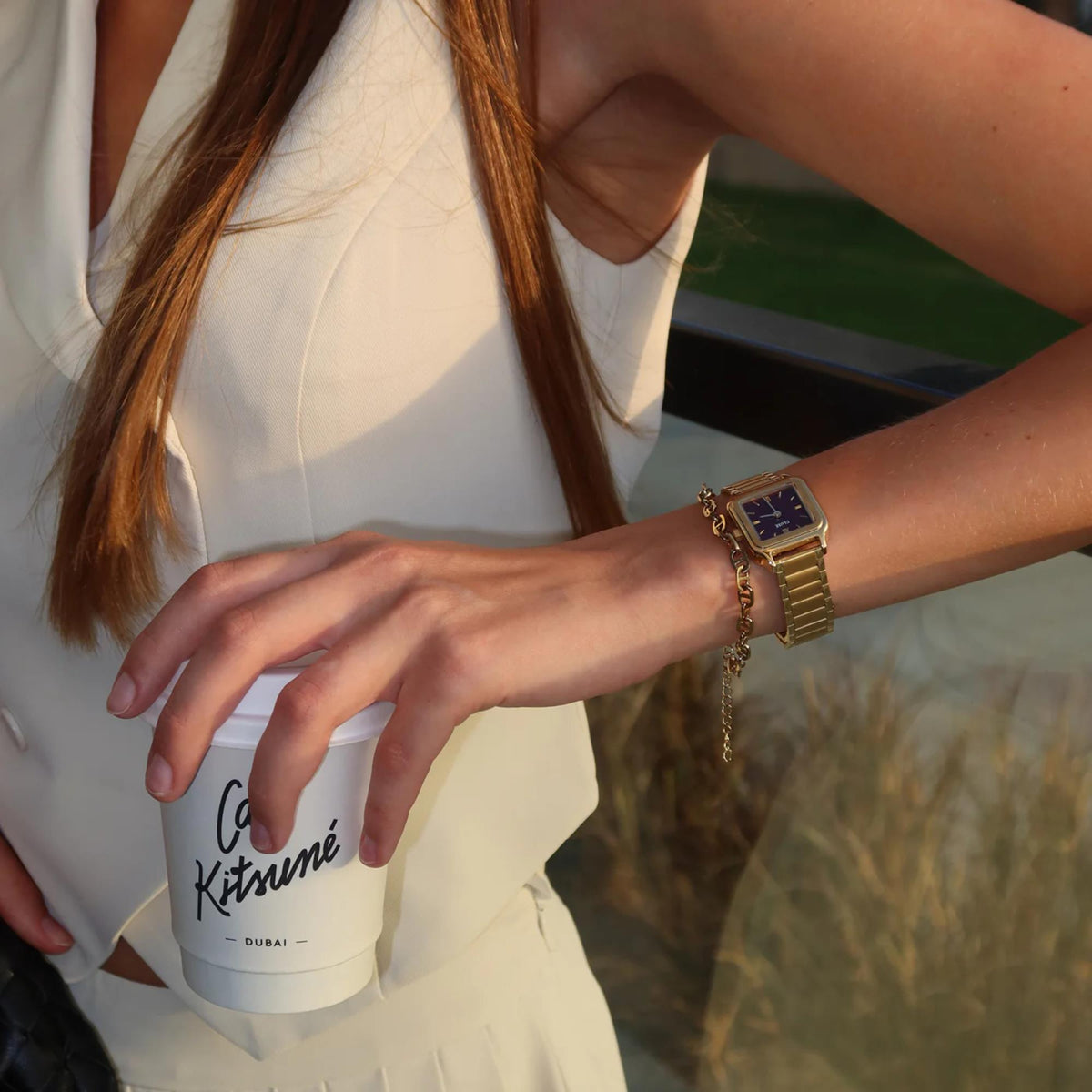 Gold-tone square watch with purple-red dial on wrist with link bracelet