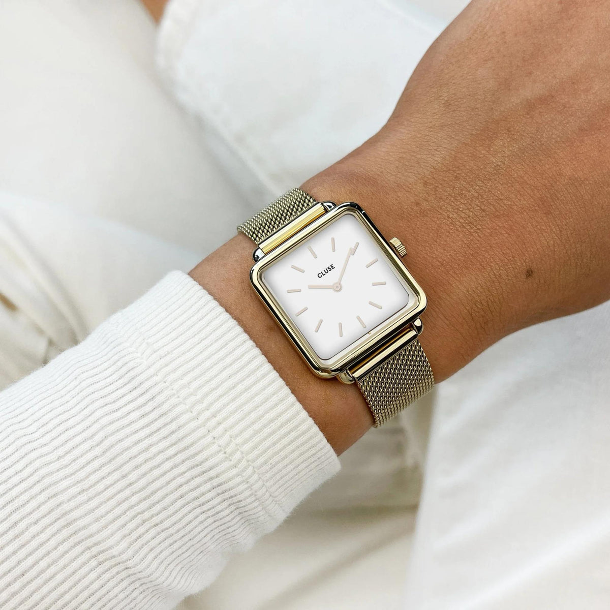 Women's square quartz watch with white dial and gold-tone mesh strap on sleeve
