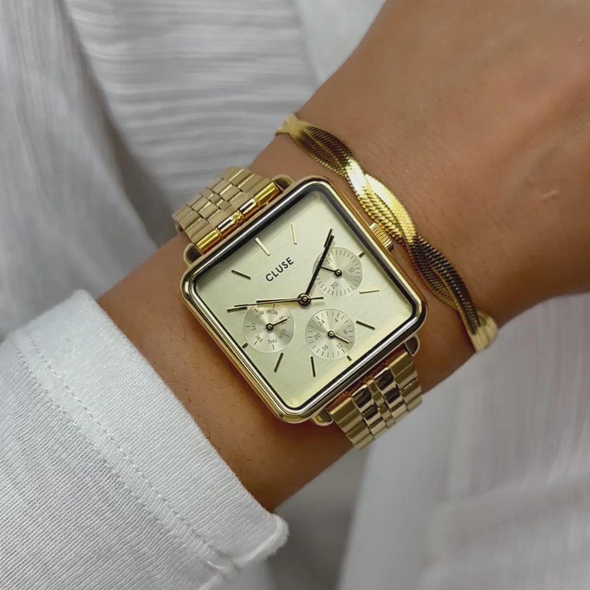 Gold-tone rectangular watch on wrist with white dial and metal bracelet