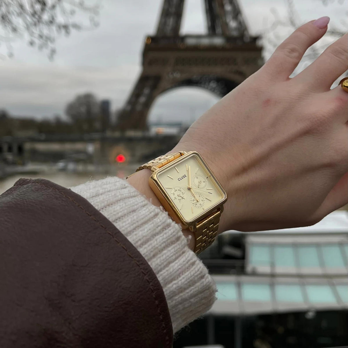 Gold-tone rectangular watch on wrist with white dial and link bracelet outdoors