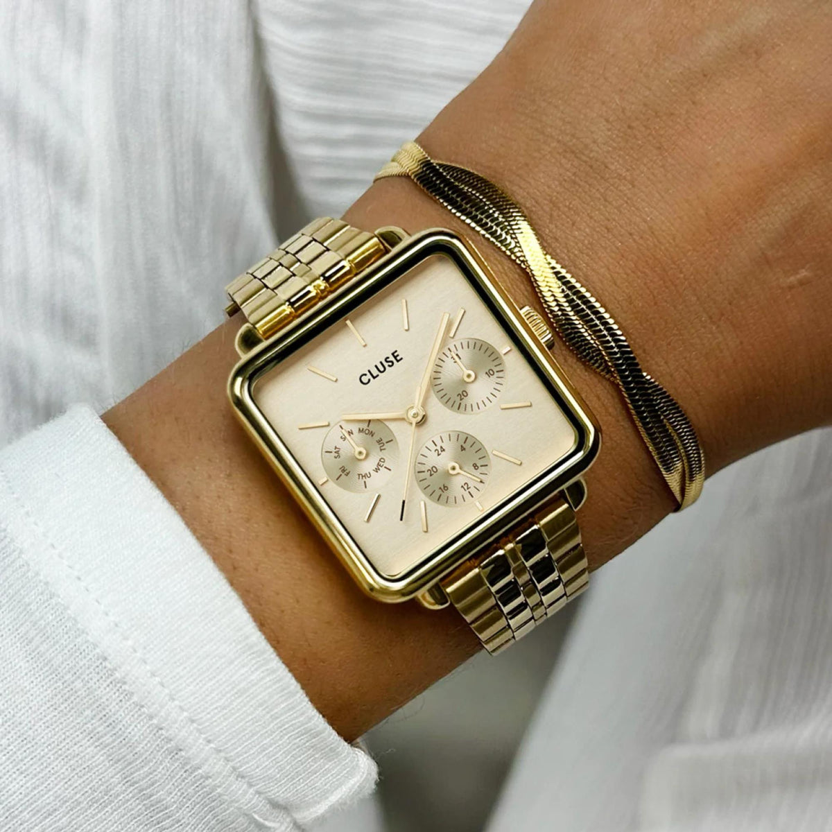 Gold-tone rectangular chronograph watch with white dial and metal bracelet on wrist