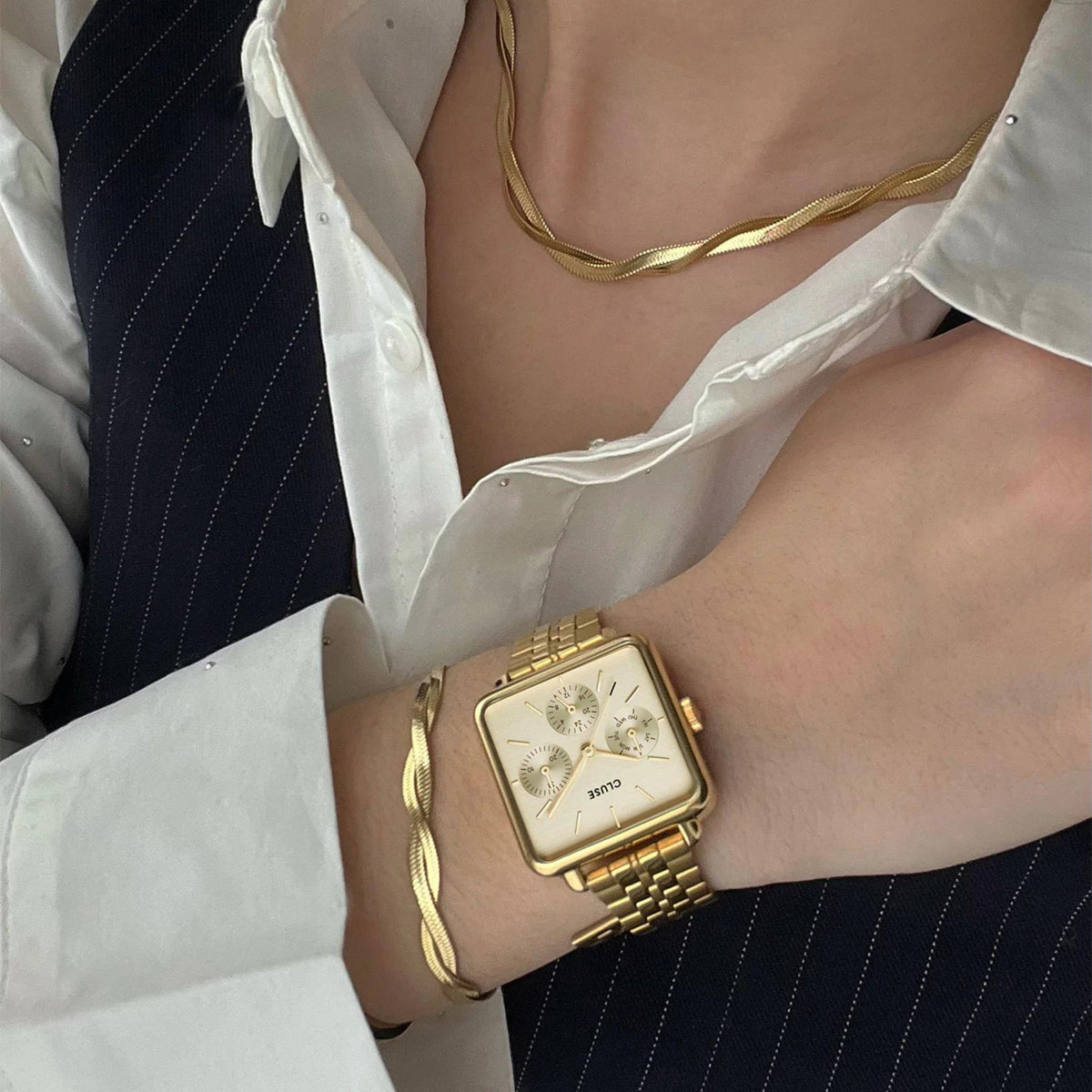 Gold-tone rectangular watch on wrist with white dial and link bracelet