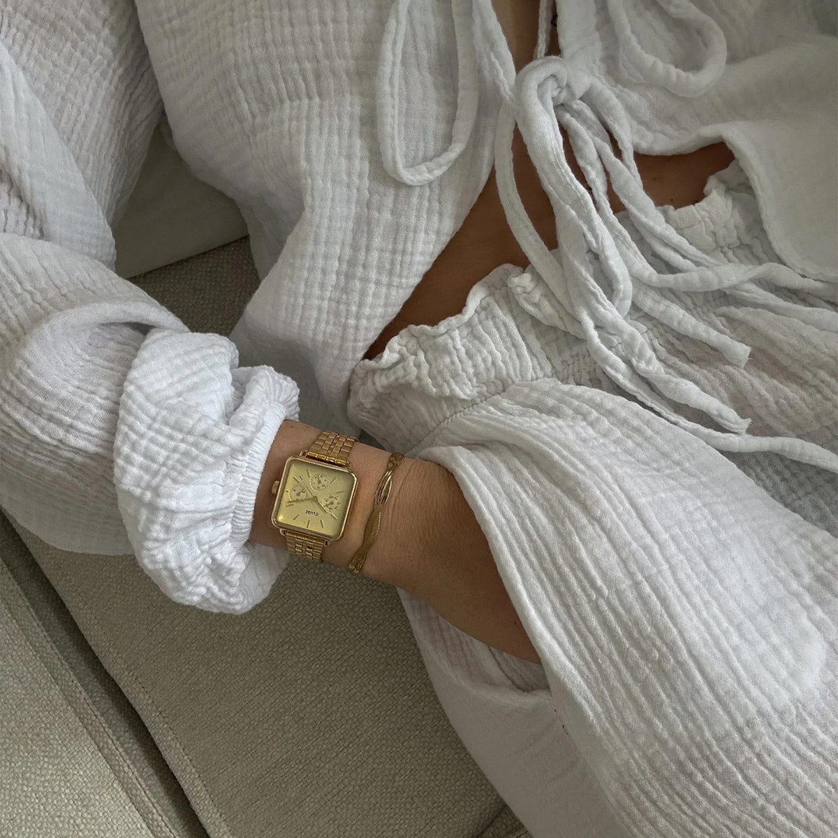 Gold-tone rectangular watch on wrist with white dial and metal bracelet