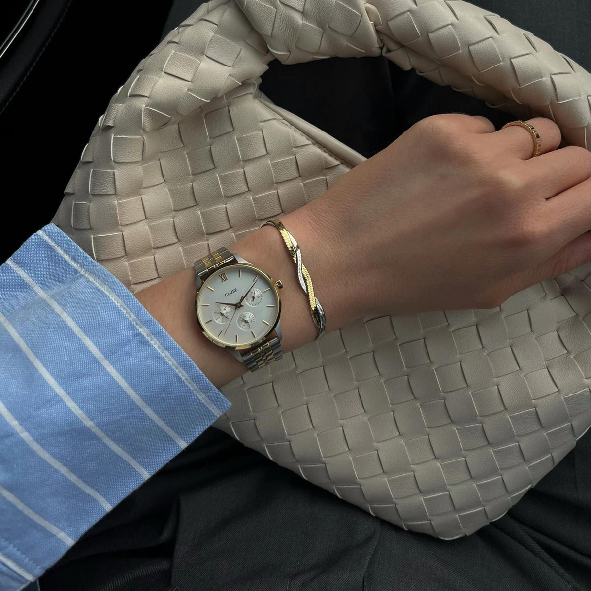 Women’s chronograph watch worn on wrist with two-tone steel band over woven bag