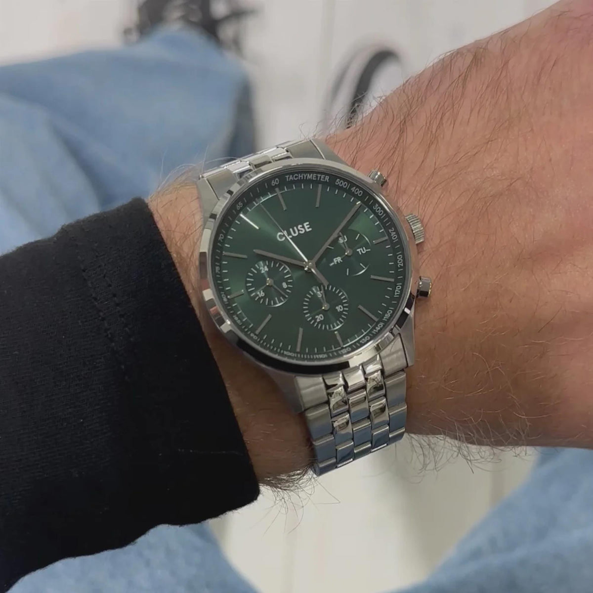 Men's quartz chronograph watch with green dial and steel bracelet on wrist in daylight.