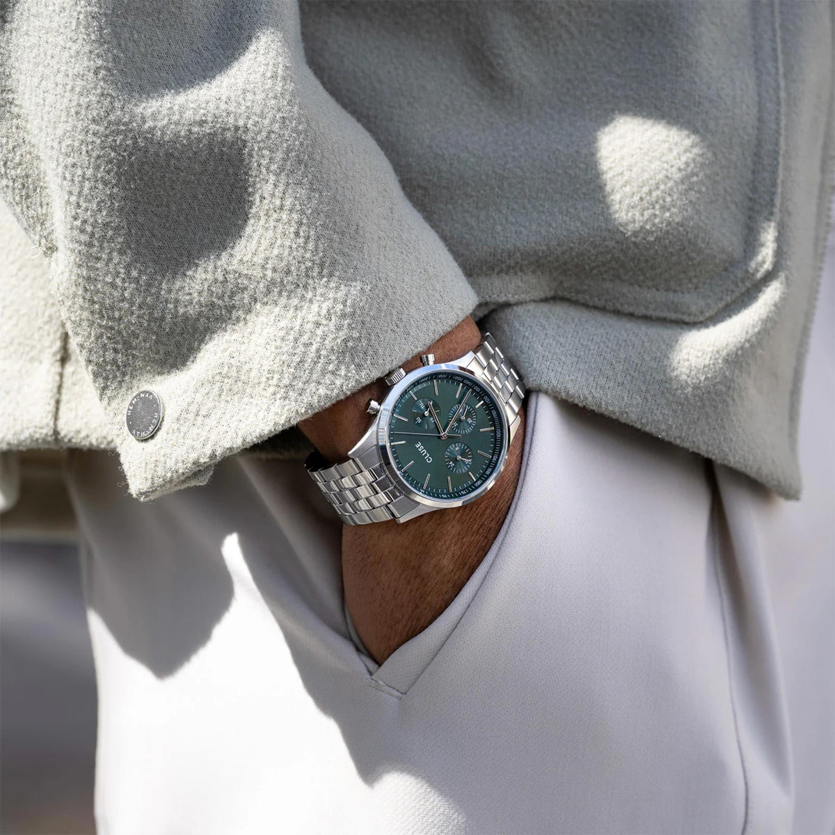 Men's quartz chronograph watch with green dial and steel bracelet on wrist under sweater cuff.