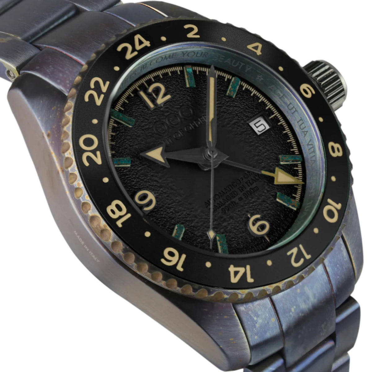 Black dial GMT watch close-up with gold hour markers, teal accents, black strap