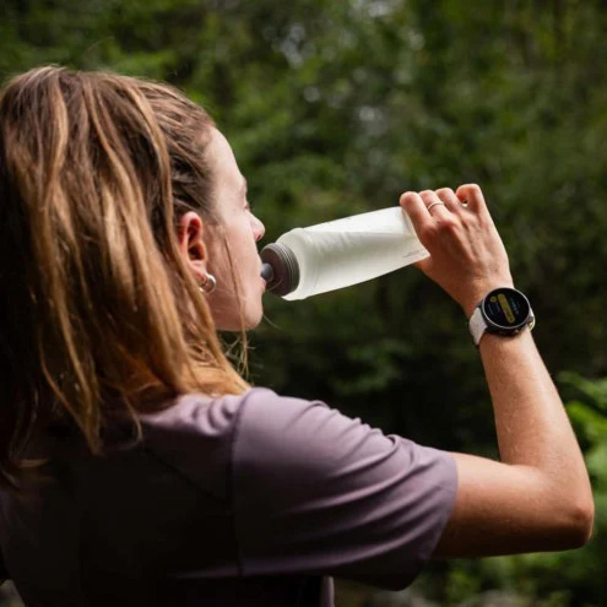 A person wearing the Suunto Race SS050932000 watch while drinking from a water bottle