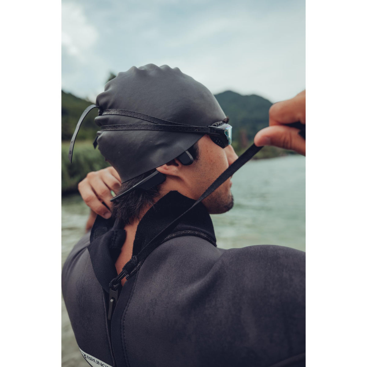 Suunto Aqua SS051023000 black sports open-ear wireless headphones worn by swimmer adjusting wetsuit collar near water