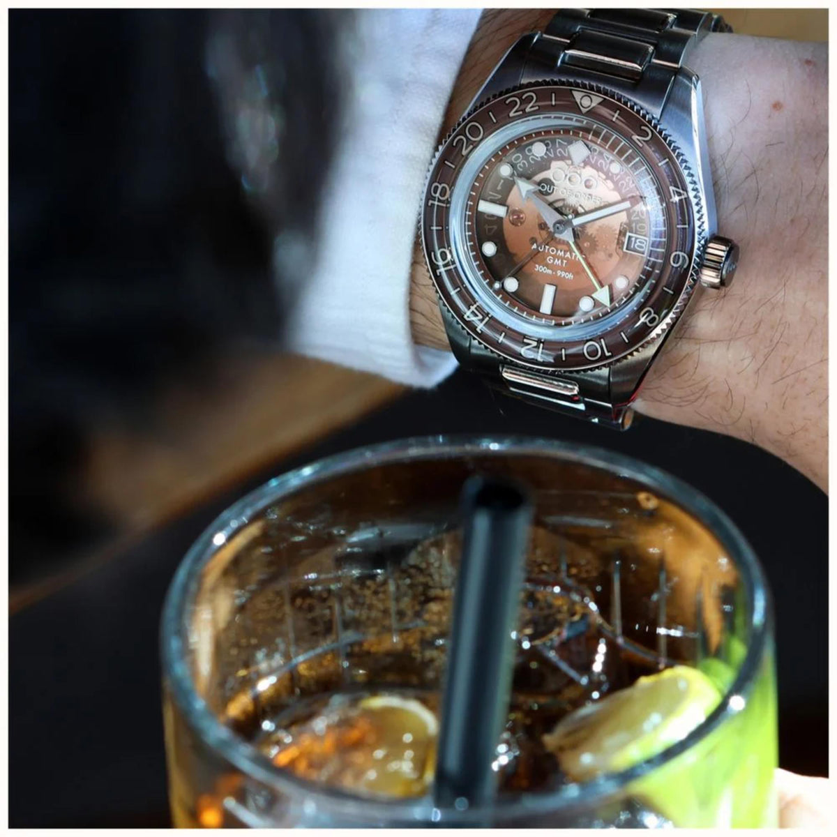 Men's automatic steel wristwatch on wrist with brown dial and metal link bracelet