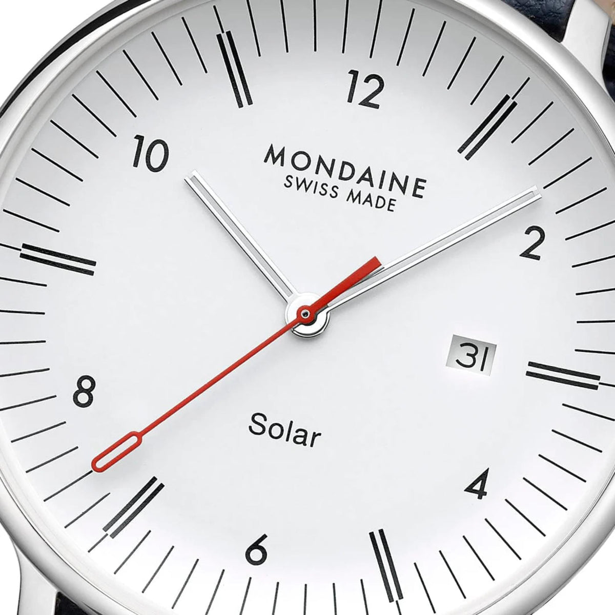 Close-up of Mondaine Doppio watch dial, showing the white face, minimalist black hour and minute markers, date window at 3 o'clock, text reading 'Mondaine Swiss Made' and 'Solar', and the signature red second hand