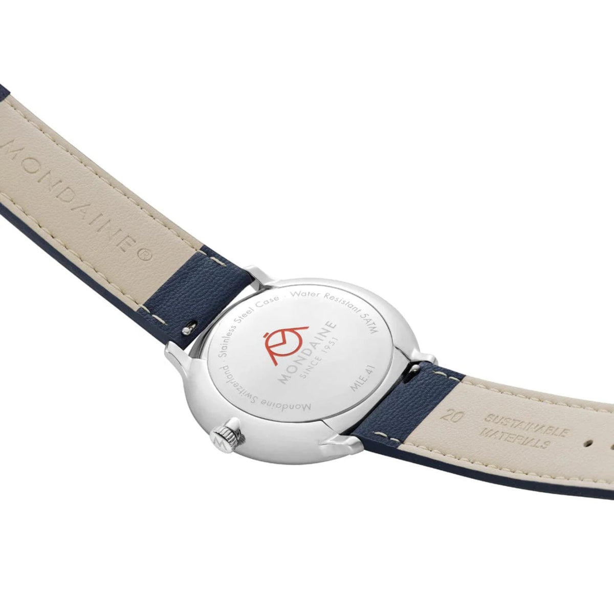 Close-up of polished silver stainless steel caseback, showing an engraved red Mondaine logo, flanked by the cream-colored interior linings of the navy blue strap