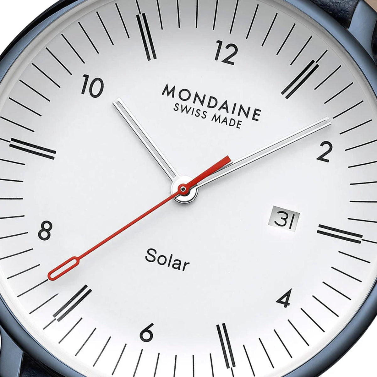 Close-up of Mondaine Doppio watch dial, showing the white face, minimalist black hour and minute markers, date window at 3 o'clock, text reading 'Mondaine Swiss Made' and 'Solar', and the signature red second hand
