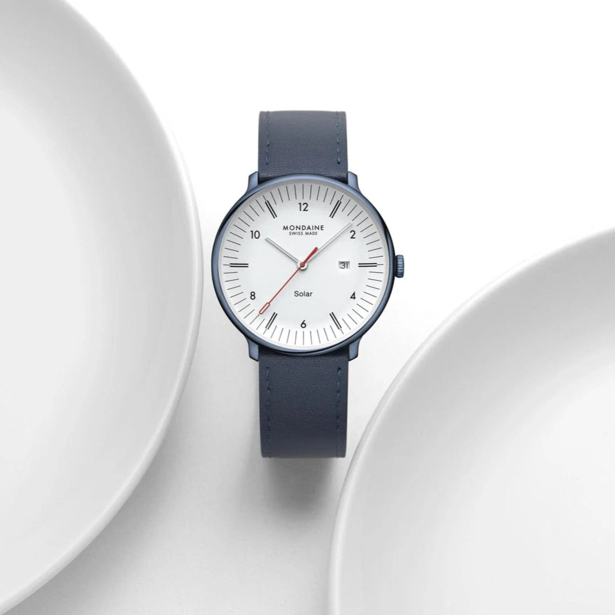 Mondaine Doppio Solar watch with its navy blue leather strap, artfully framed between the curved white edges of two ceramic plates