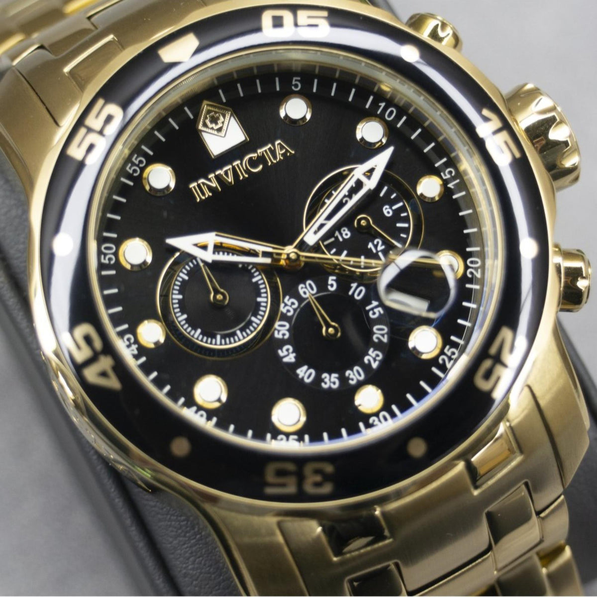 Close-up of Invicta Pro Diver chronograph face: black dial, gold hands, subdials.