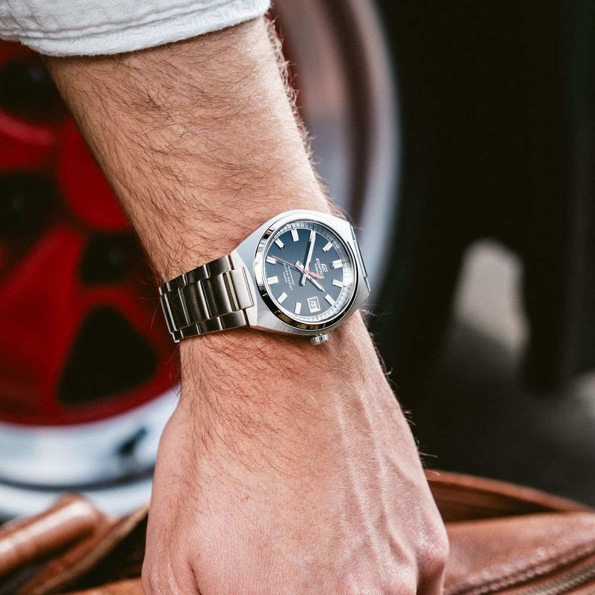 Casio Edifice EFB-109D-1AVEF steel watch worn on a wrist outdoors next to a leather bag