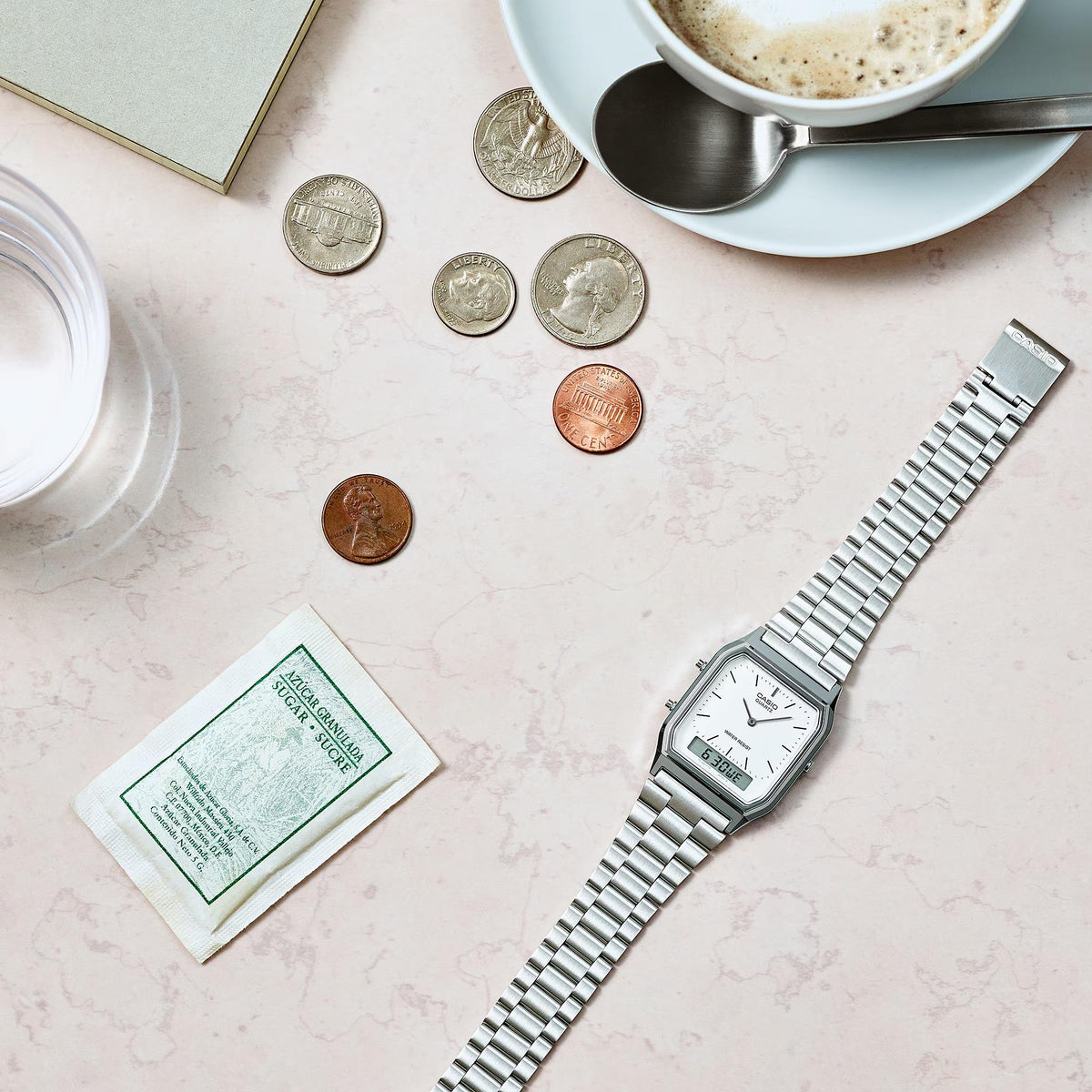 Steel bracelet quartz watch with white dial, angled view on countertop with coins
