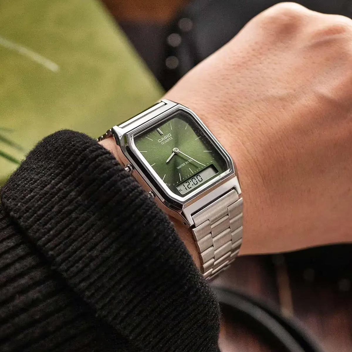 Green dial Casio quartz watch with stainless steel bracelet on wrist, angled close-up