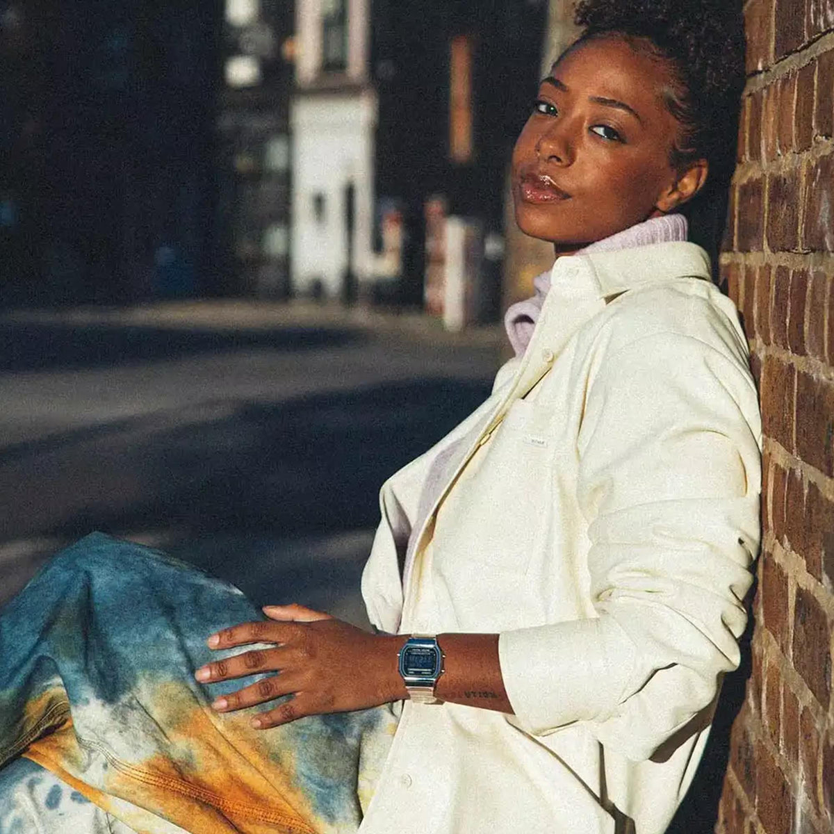 Lifestyle portrait of a woman leaning against a brick wall while wearing the Casio Vintage Quartz Digital Resin Strap Watch A168XES-1BEF