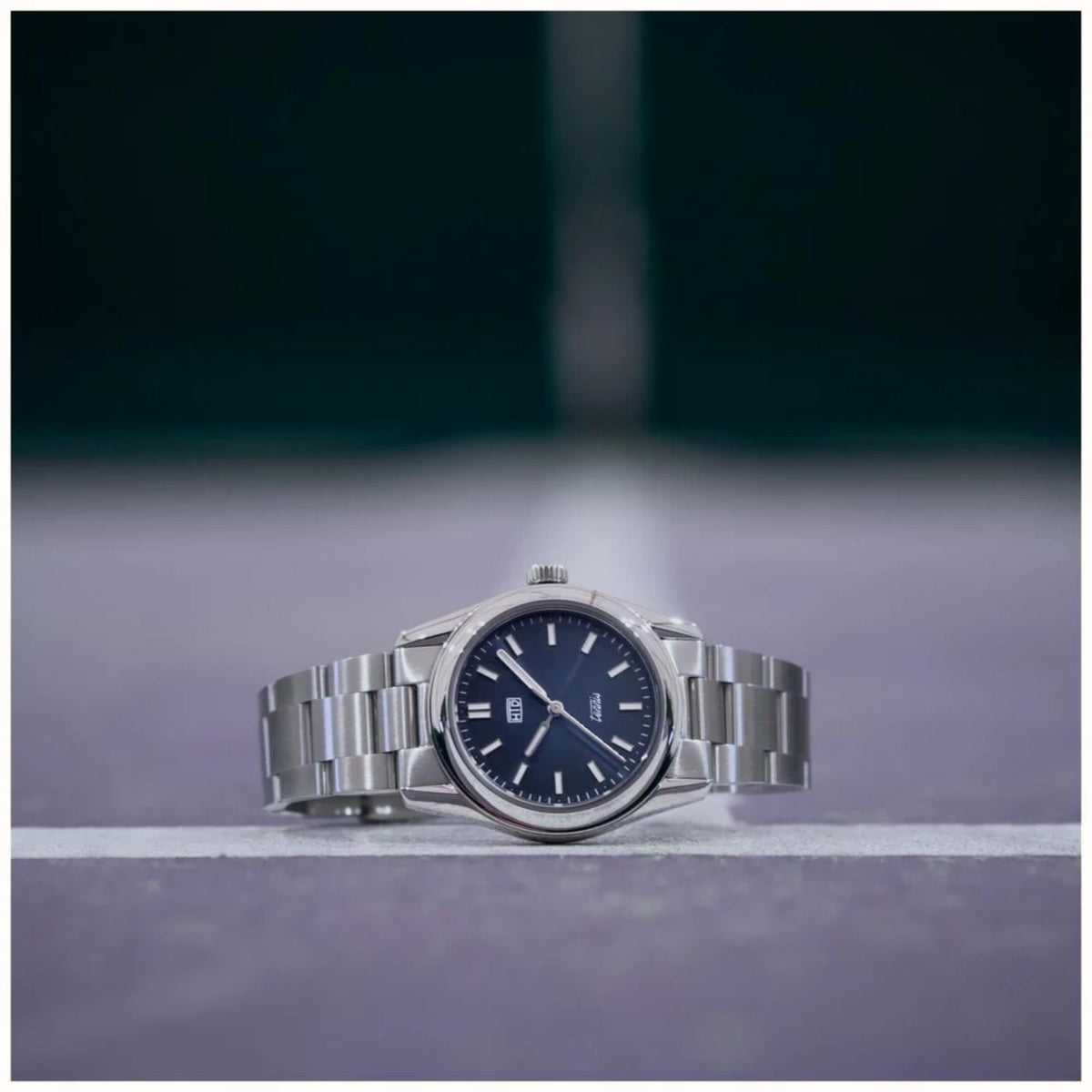 Blue dial sports watch with stainless steel bracelet, side view on ground