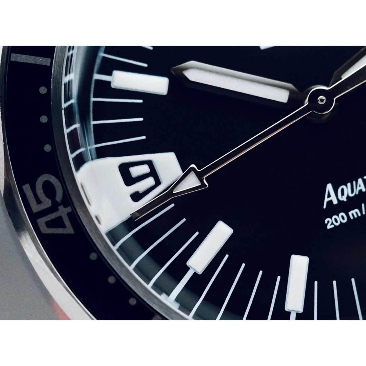 Macro view of black dial with white hour markers and metal hands on steel case