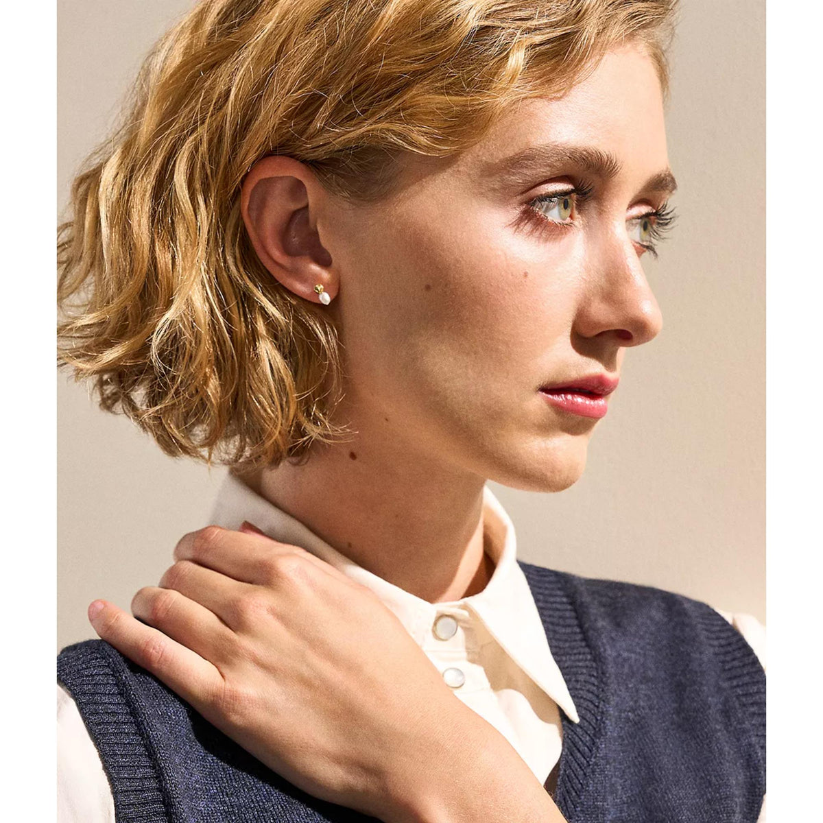 Gold-tone and white pearl stud earrings on side profile ear, visible silver posts