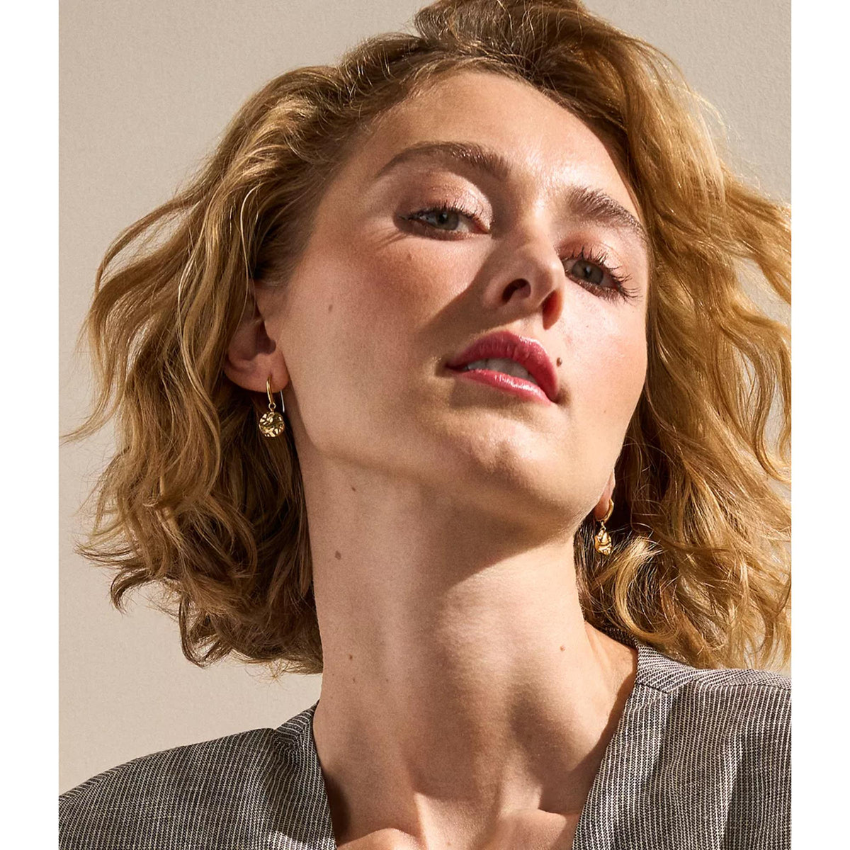 Gold-tone wave medallion drop earrings on model, dangling from small hooks