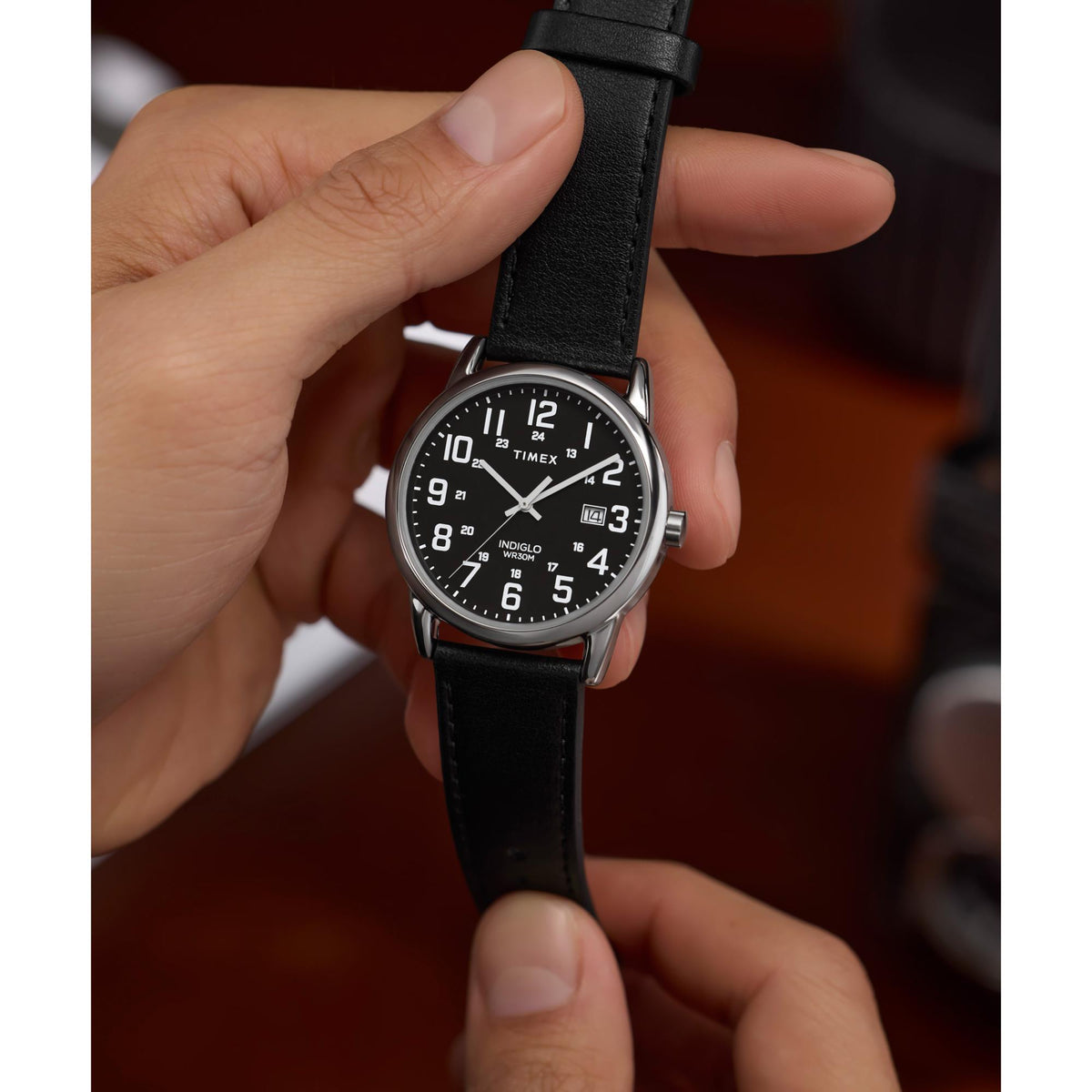 Men's quartz watch with black dial and black leather strap on open palm, silver case