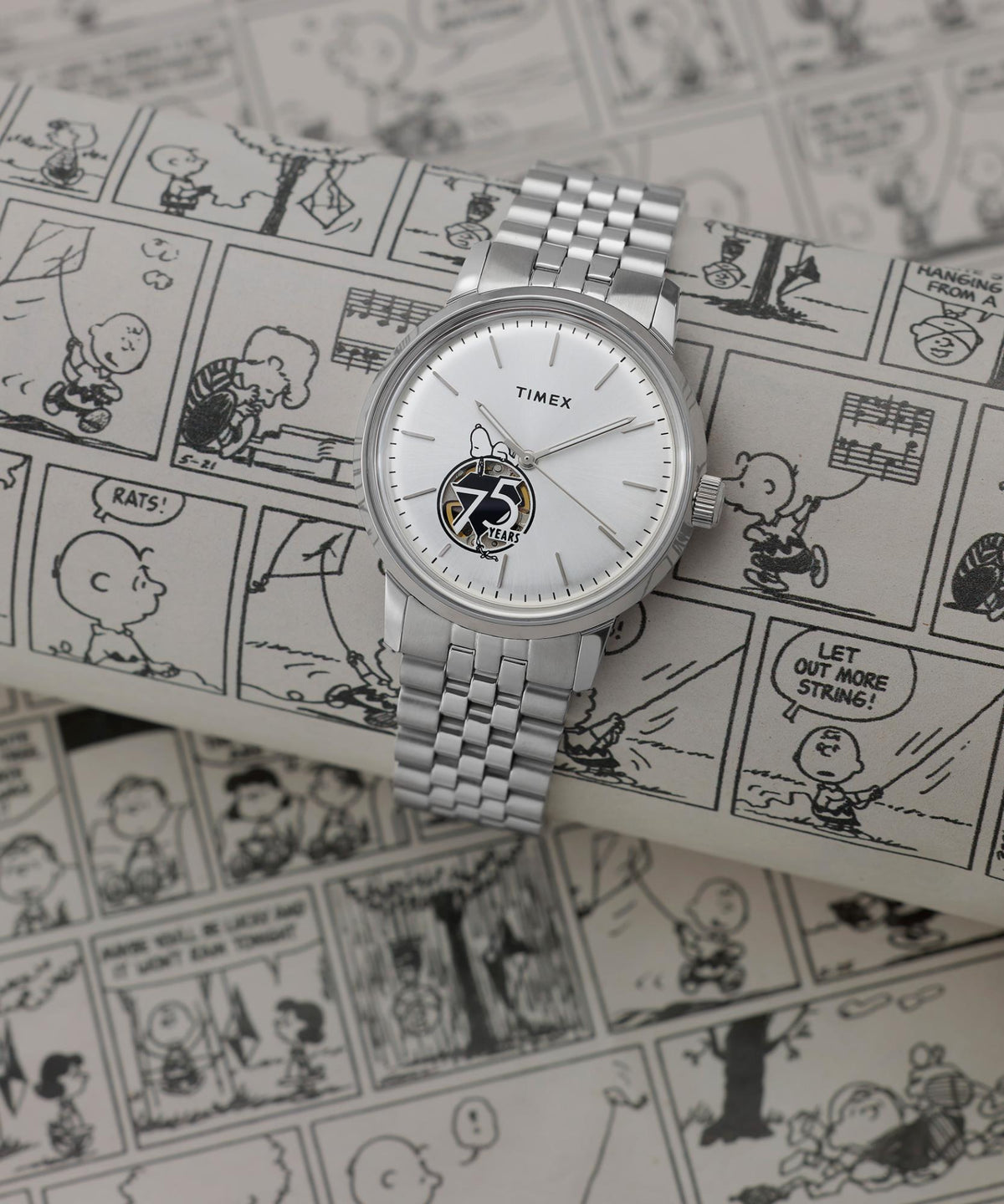 Silver steel wristwatch with white dial resting on Snoopy-themed comic print