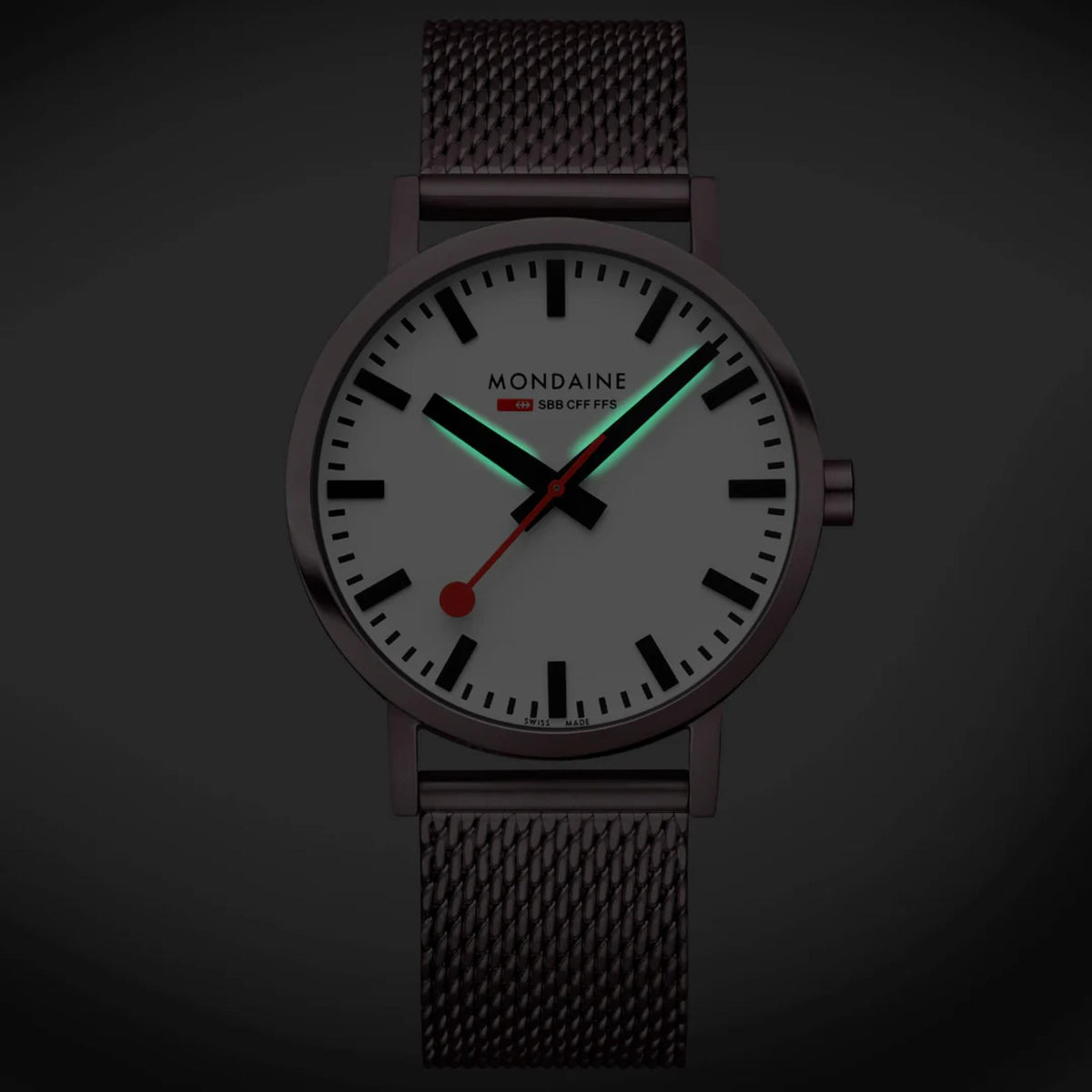 Mondaine Classic A660.30360.1BSBZ analog watch in low light, displaying green luminous hands