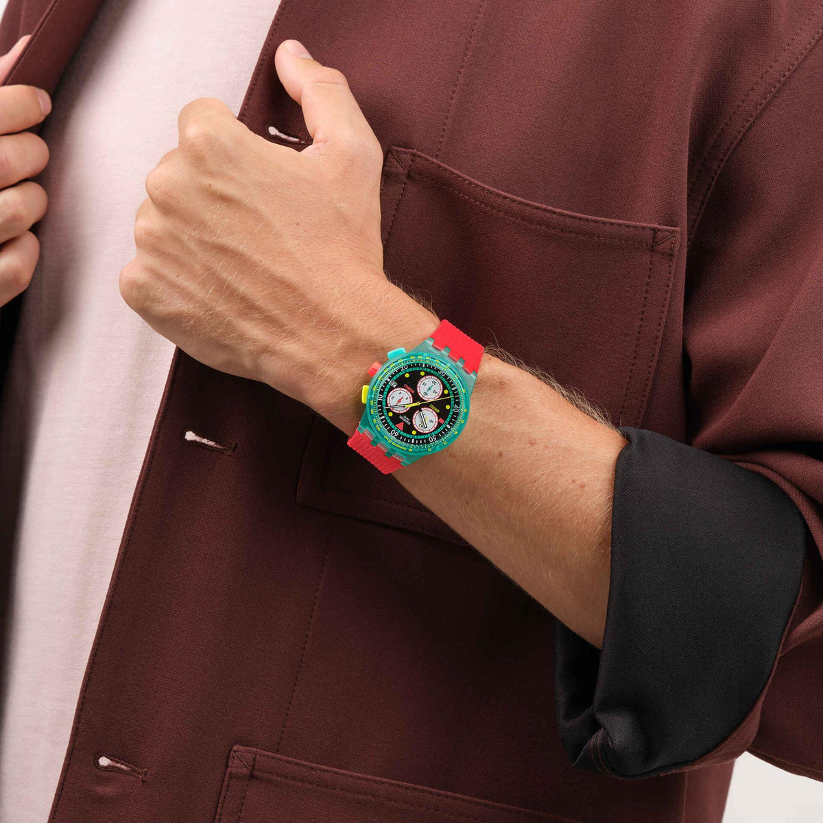 Swatch chronograph wristwatch worn on wrist; black dial, teal case, red silicone strap.