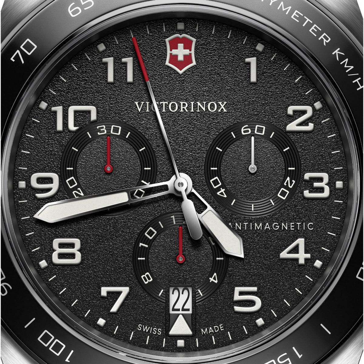 Close-up of black chronograph dial with tachymeter scale, three subdials, and red accents