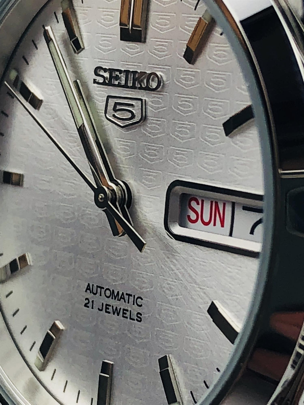 Close-up shot of the Seiko 5 SNK355K1 silver dial focusing on the applied metallic logo and textured surface details