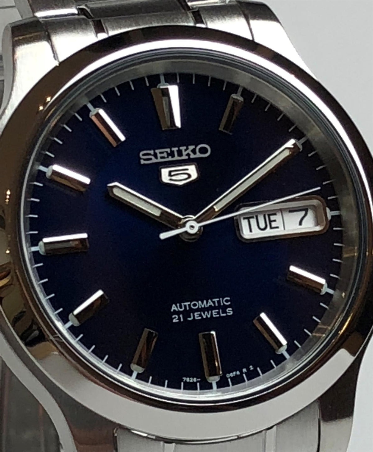 Stainless steel men's automatic watch close-up: dark blue dial, baton markers, and TUE 7 day-date