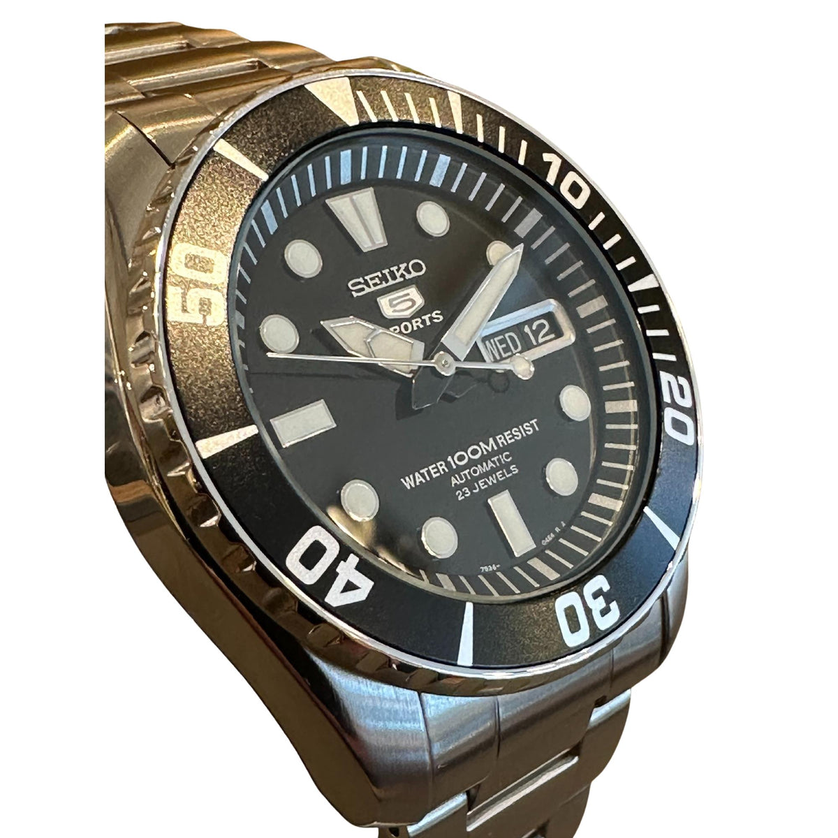 Angled view of men’s watch with dark dial, diver bezel, and metal bracelet, date window visible