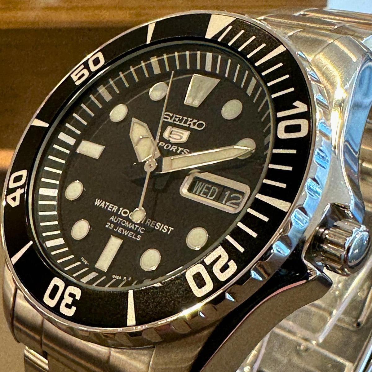 Men's Seiko Sports watch with black dial, stainless bracelet, and date window at 12