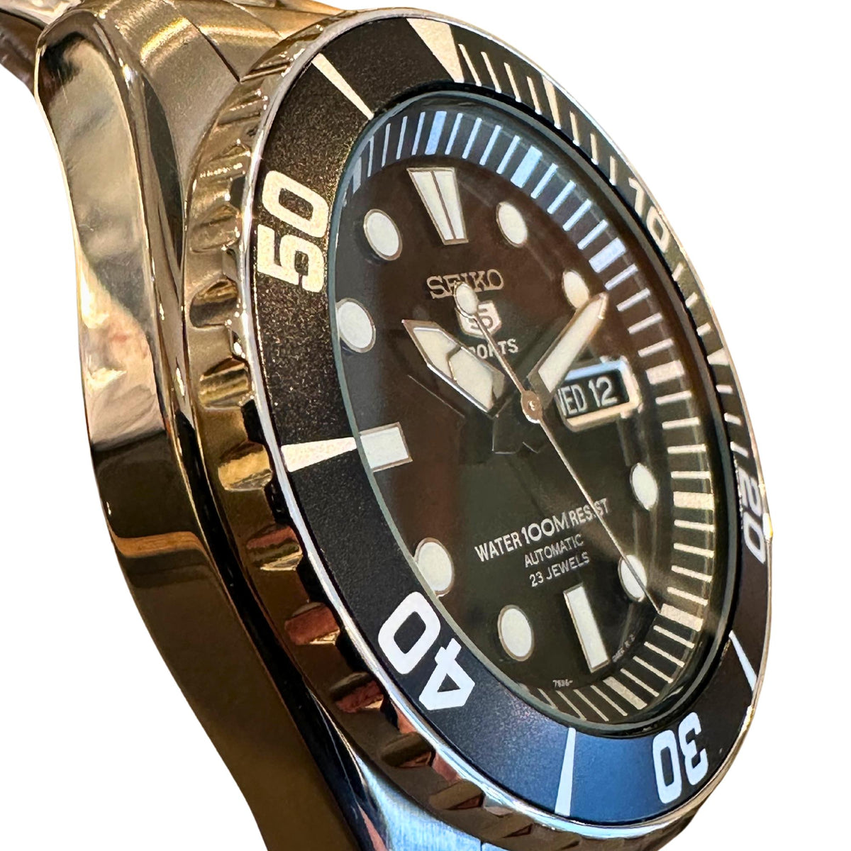 Black Seiko Sports watch dial with date window reading WED 12 and bold hour markers