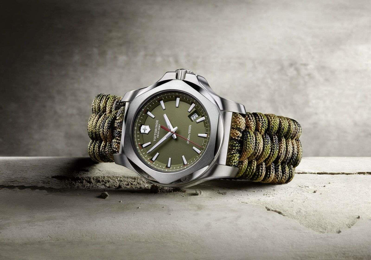 Men's stainless steel watch with dark green face and olive-green paracord strap, three-quarter view.