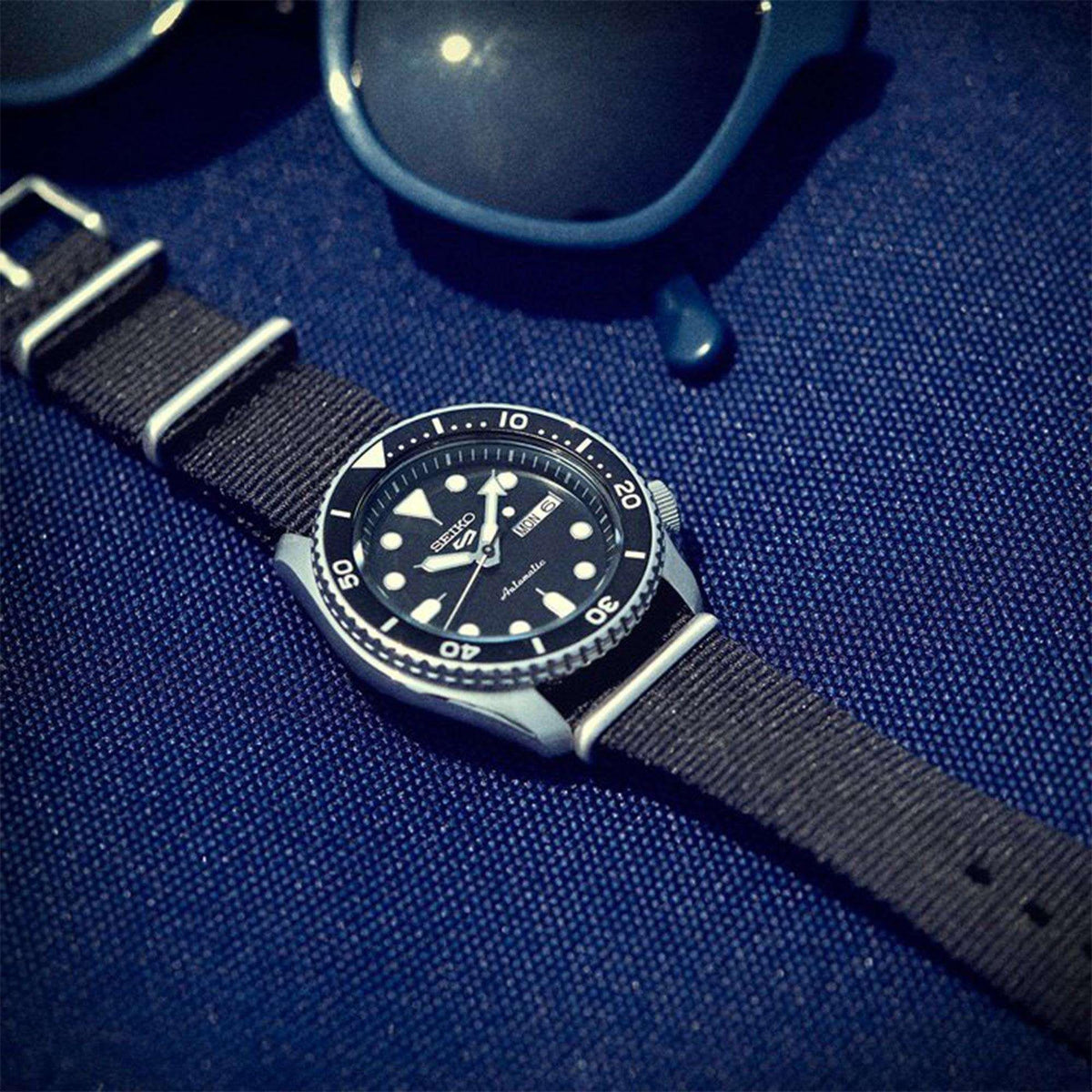 Men's automatic dive watch with black dial, metal bezel, and black fabric strap.