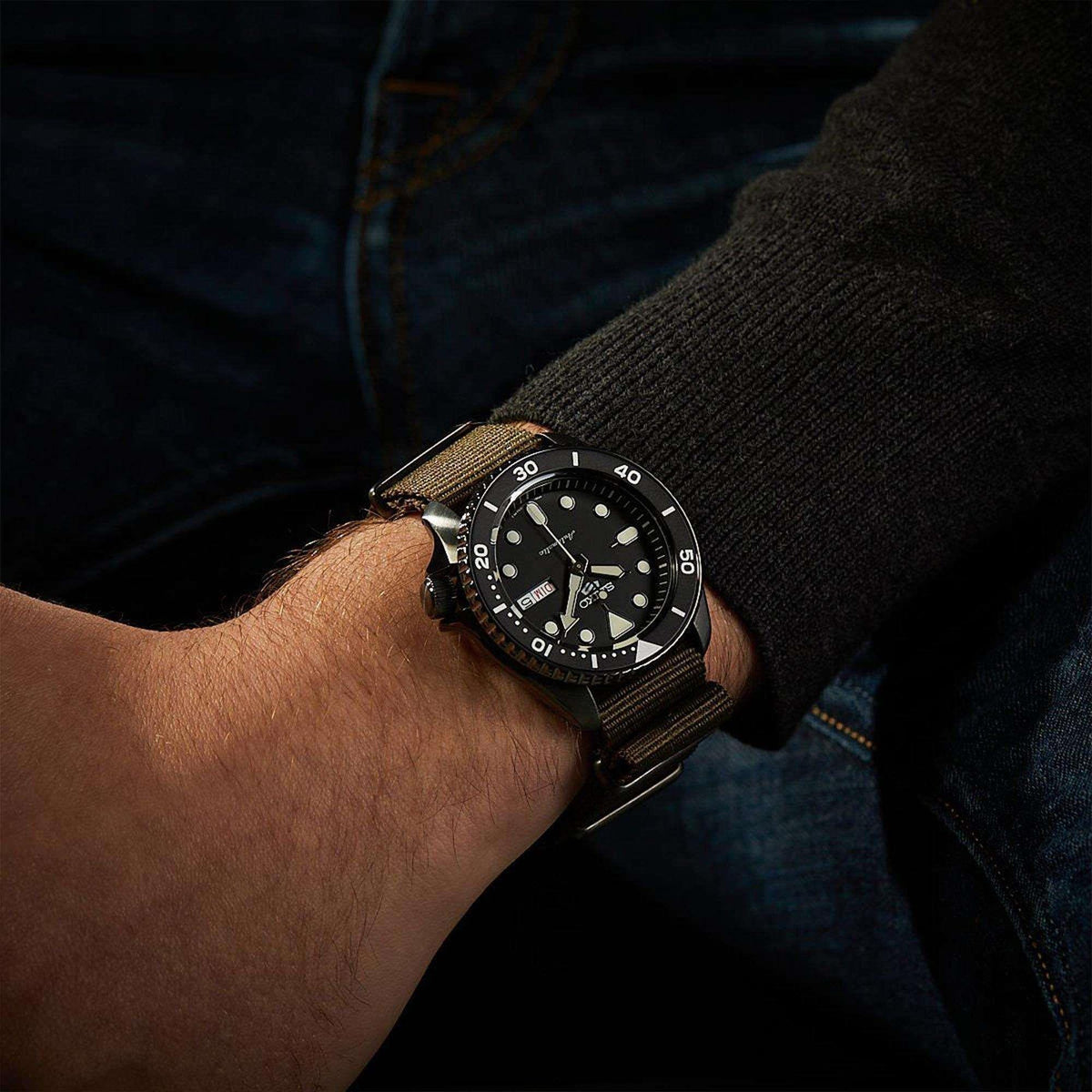 Men's automatic wristwatch on wrist with black dial and olive-green NATO strap