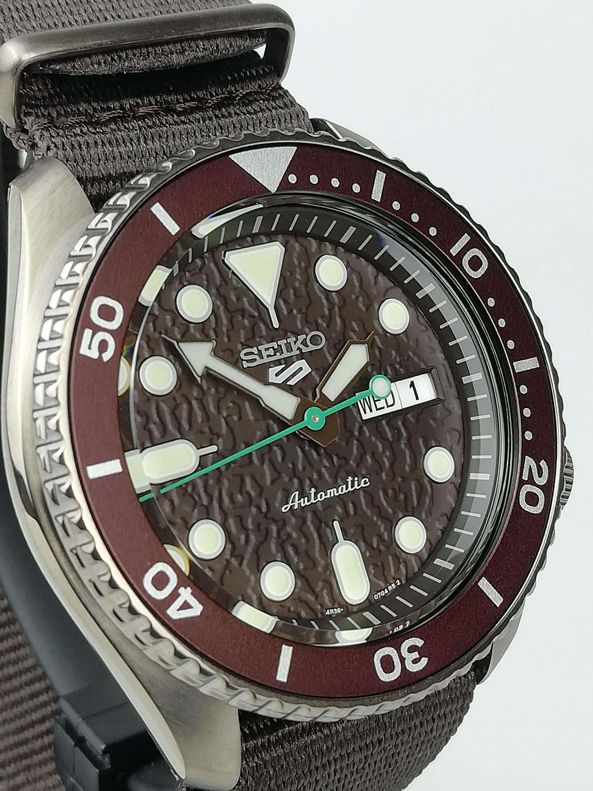 Seiko 5 Sports close-up with brown dial, stainless bezel, day-date window, brown fabric strap