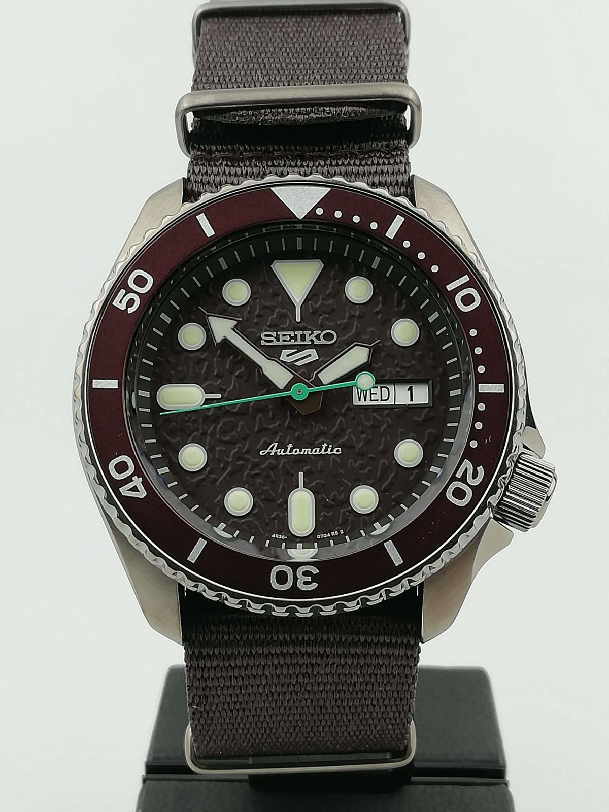 Seiko 5 Sports watch front view with stainless case, brown dial, and brown canvas strap