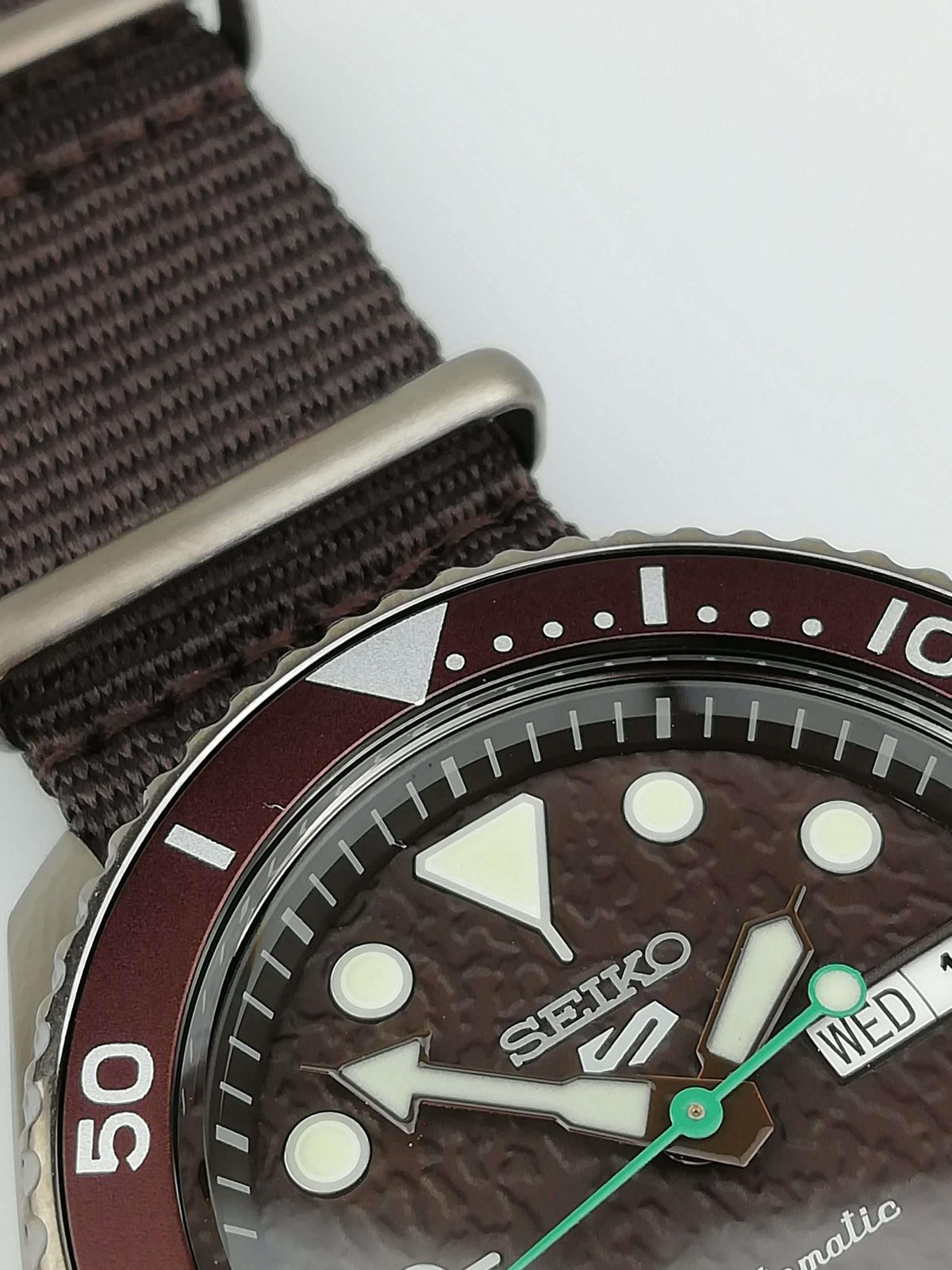 Men's Seiko 5 Sports watch dial with day/date Wed 1, brown strap, maroon bezel