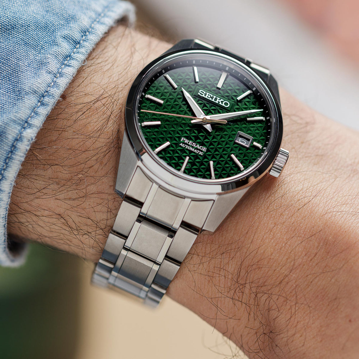 Men's automatic watch on wrist with green dial and silver stainless bracelet, crown visible
