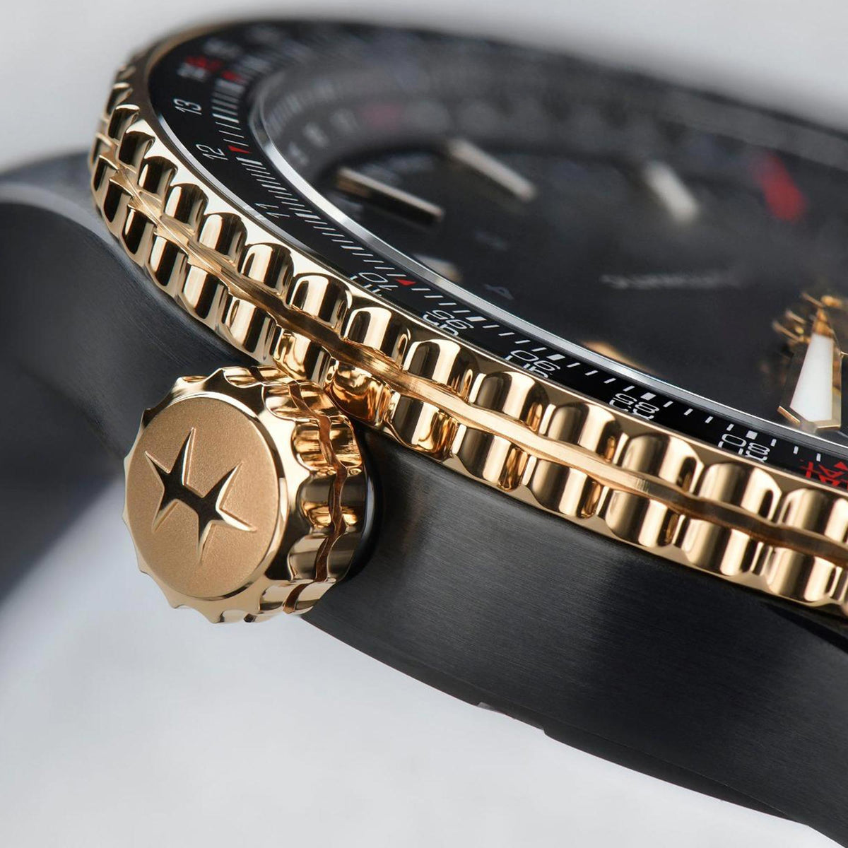 Men's automatic watch detail: gold-tone ridged bezel, gold crown, black leather strap.