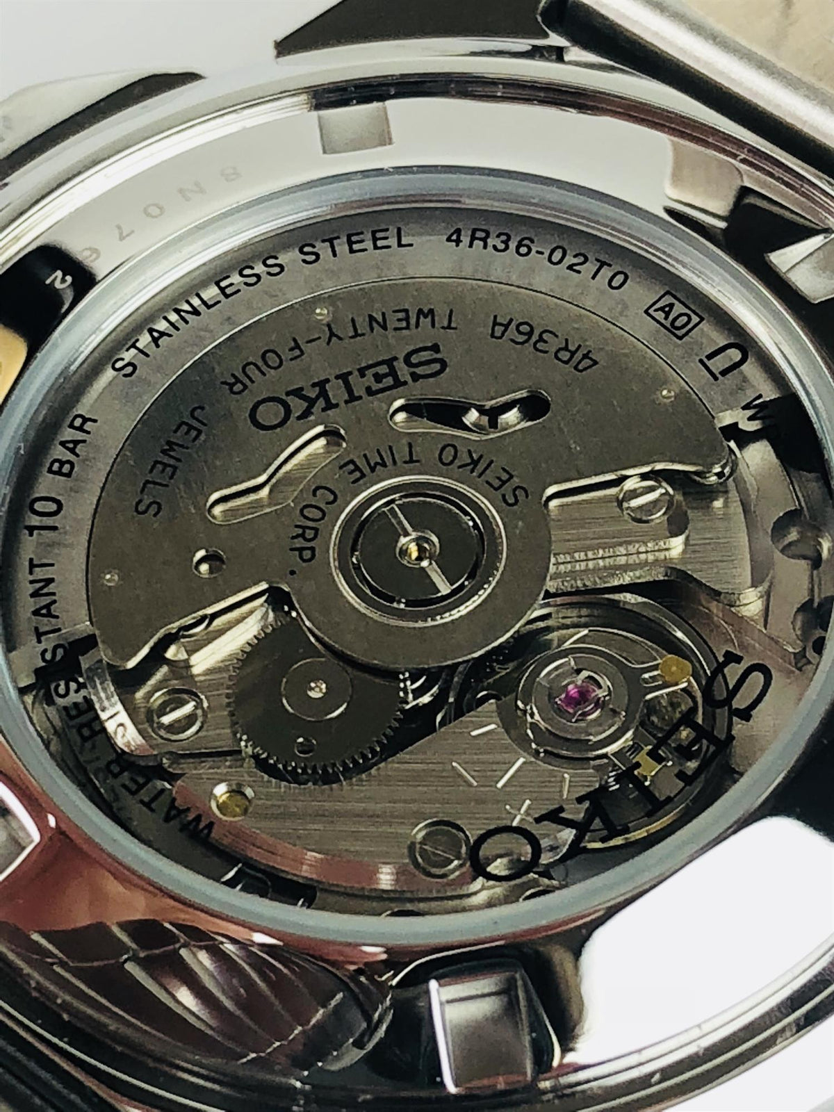 Stainless steel watch case back with engraved markings and mechanical movement view.
