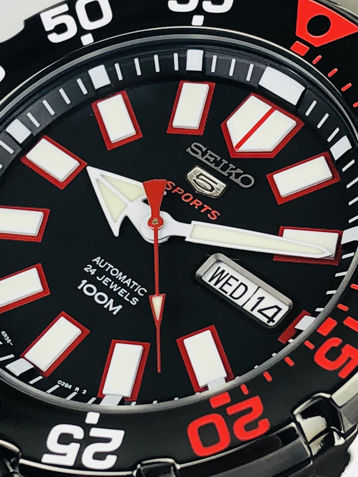 Seiko Sports dial close-up: black face, white markers, red hands, WED 14 date.