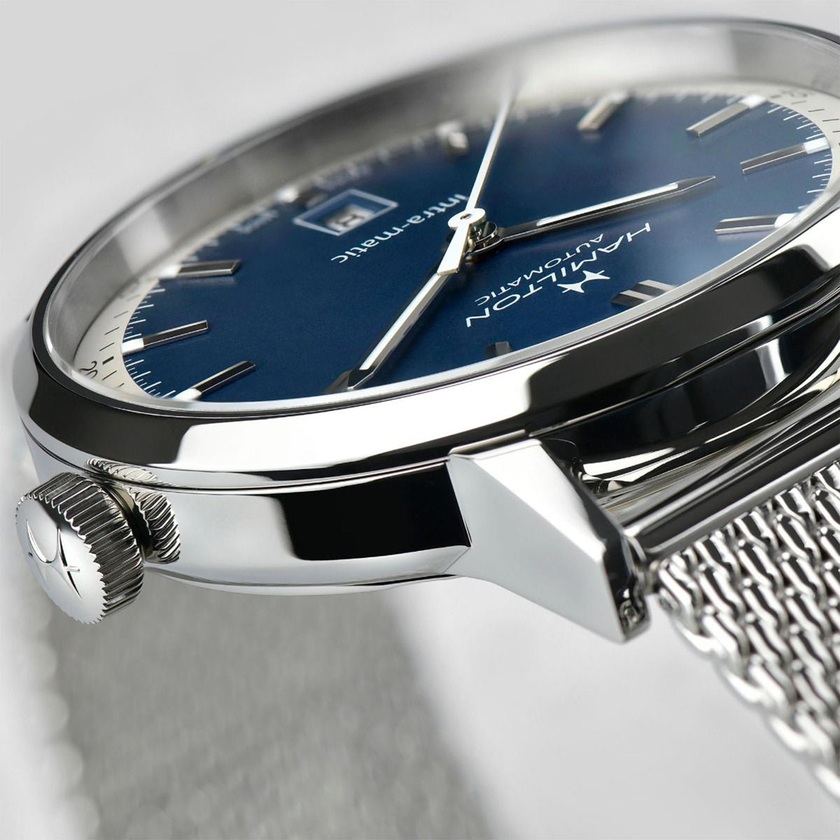 Men's steel automatic watch, close-up blue dial, crown detail and mesh strap