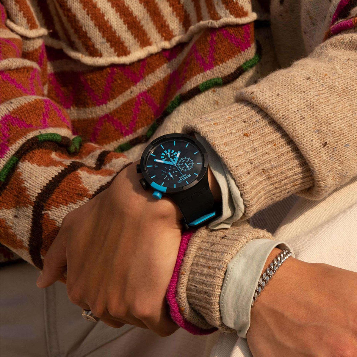 Black wristwatch with blue-accent dial and black silicone strap worn over a knit sleeve