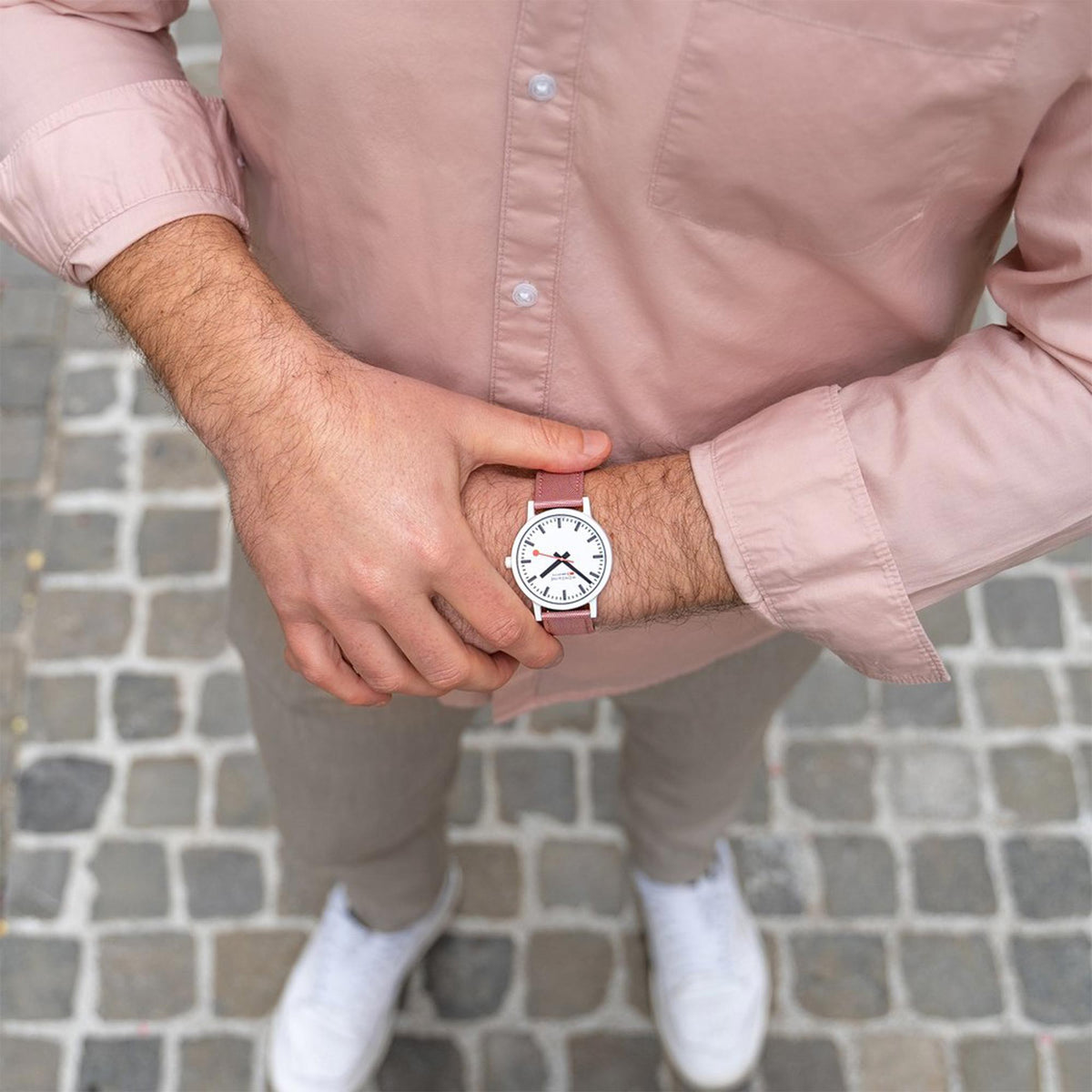 Watch on wrist outdoors with white dial, black numerals, and pink textile band